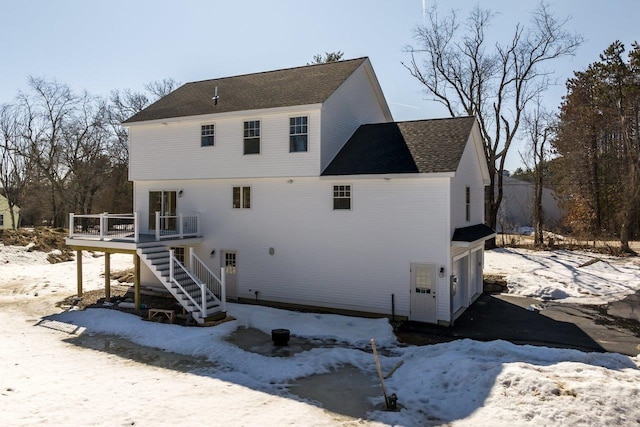 snow covered house featuring stairway, a garage, and a deck