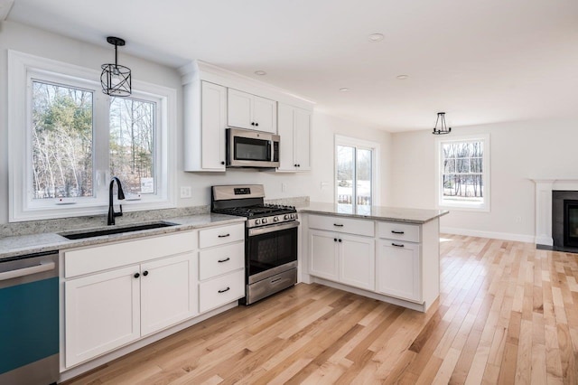 kitchen featuring a fireplace with flush hearth, a sink, appliances with stainless steel finishes, a peninsula, and white cabinets