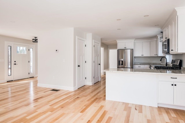 kitchen featuring light stone counters, appliances with stainless steel finishes, white cabinets, and light wood finished floors