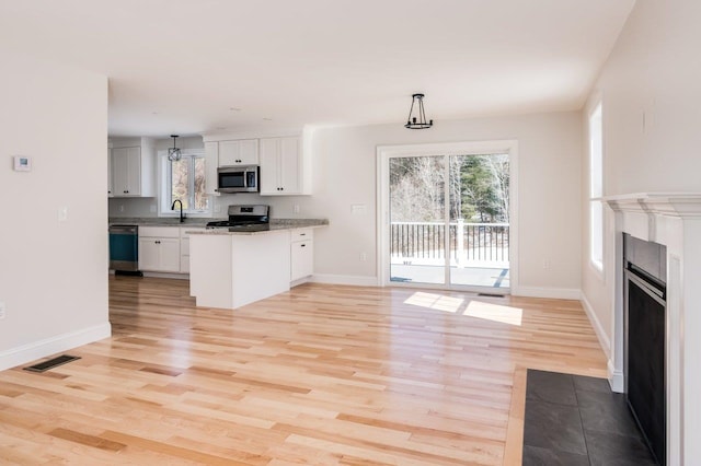 kitchen featuring visible vents, appliances with stainless steel finishes, a peninsula, white cabinets, and a sink