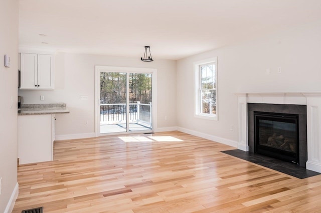 unfurnished living room with visible vents, light wood-style floors, baseboards, and a tile fireplace