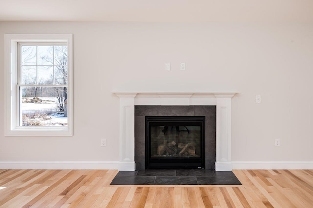 room details featuring a tiled fireplace, wood finished floors, and baseboards