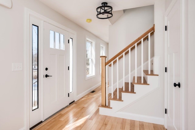 entrance foyer with stairway, baseboards, visible vents, and light wood finished floors