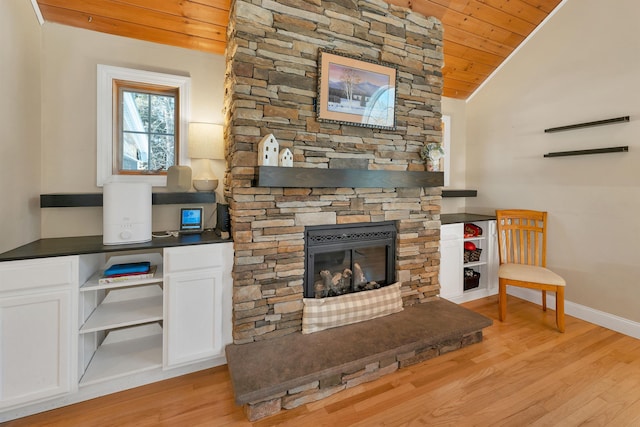 living room featuring baseboards, wood ceiling, vaulted ceiling, a stone fireplace, and light wood-style floors