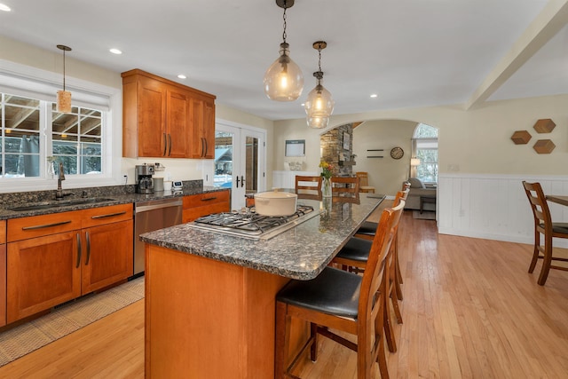 kitchen with a wainscoted wall, a sink, arched walkways, appliances with stainless steel finishes, and light wood finished floors