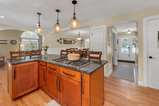 kitchen featuring light wood-type flooring, arched walkways, hanging light fixtures, and stainless steel gas cooktop