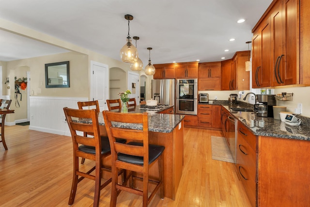 kitchen featuring arched walkways, light wood-type flooring, stainless steel appliances, and a kitchen bar