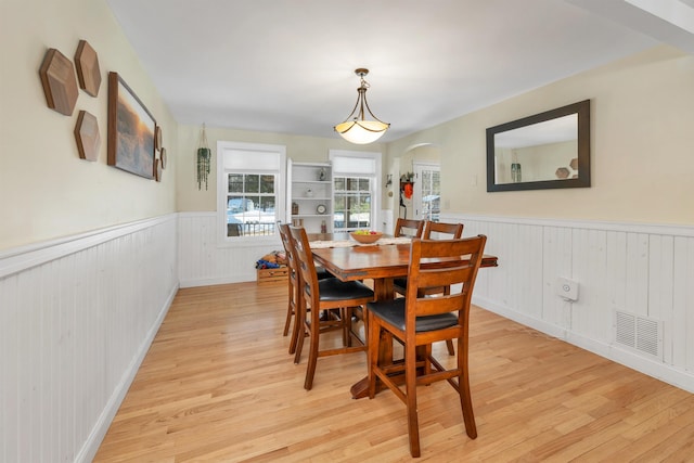 dining room featuring a wainscoted wall, arched walkways, visible vents, and light wood finished floors