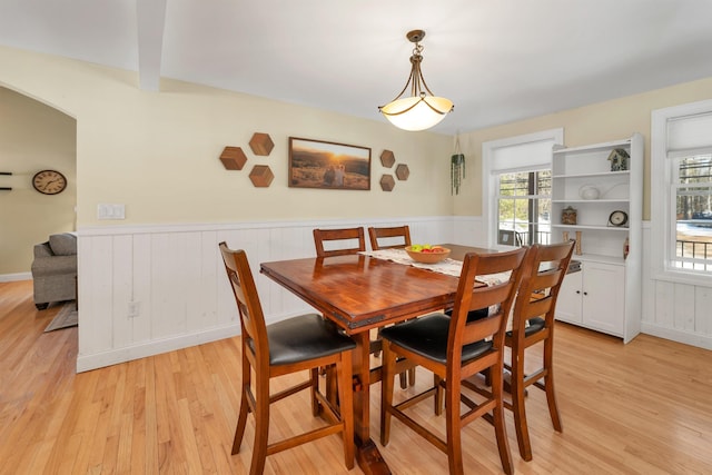 dining space with arched walkways, a wainscoted wall, and light wood-style flooring