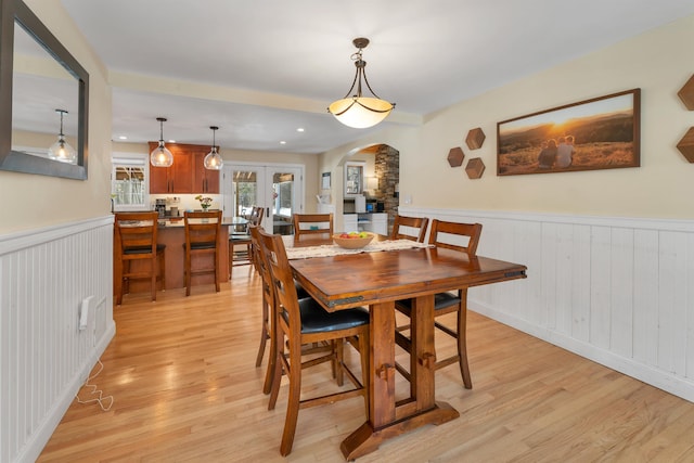 dining area featuring arched walkways, wainscoting, french doors, and light wood-style flooring