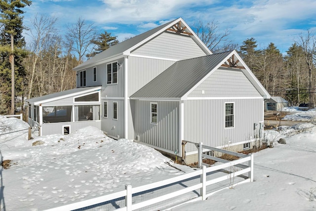 snow covered rear of property with fence and a sunroom