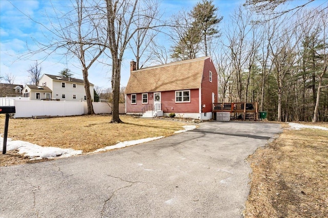 dutch colonial with fence, driveway, a gambrel roof, a chimney, and a deck