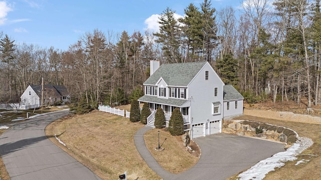 view of front of home with driveway, covered porch, an attached garage, a shingled roof, and a chimney