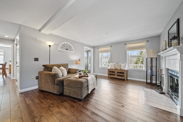 living area featuring baseboards, a fireplace with flush hearth, beamed ceiling, and wood finished floors