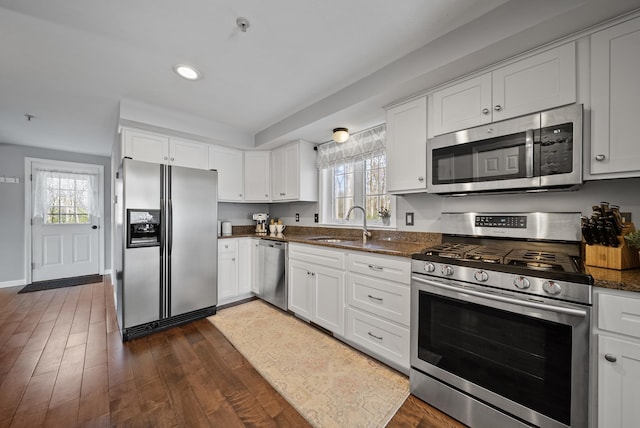 kitchen featuring dark stone countertops, dark wood-style floors, a sink, white cabinets, and appliances with stainless steel finishes