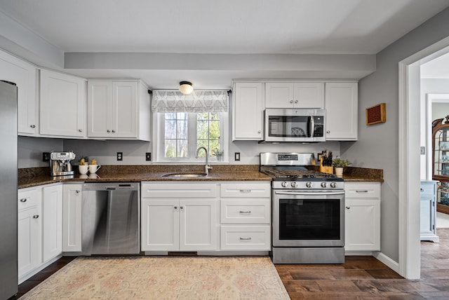 kitchen featuring dark stone counters, appliances with stainless steel finishes, dark wood-style floors, white cabinets, and a sink