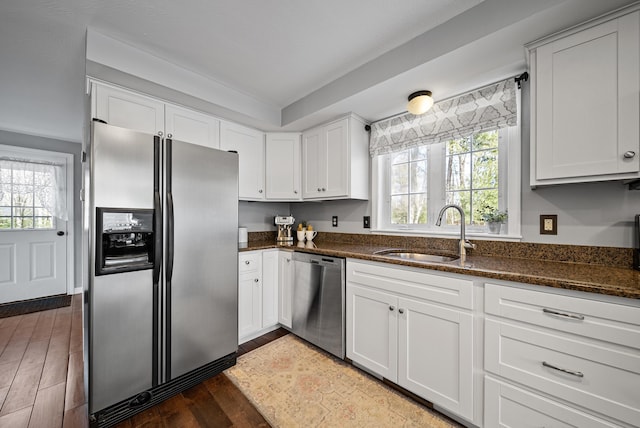 kitchen featuring wood finished floors, dark stone countertops, stainless steel appliances, and a sink