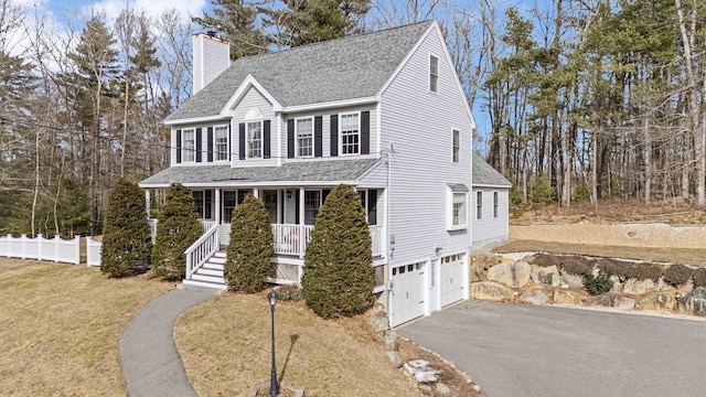 colonial house with a front yard, covered porch, a shingled roof, a chimney, and aphalt driveway