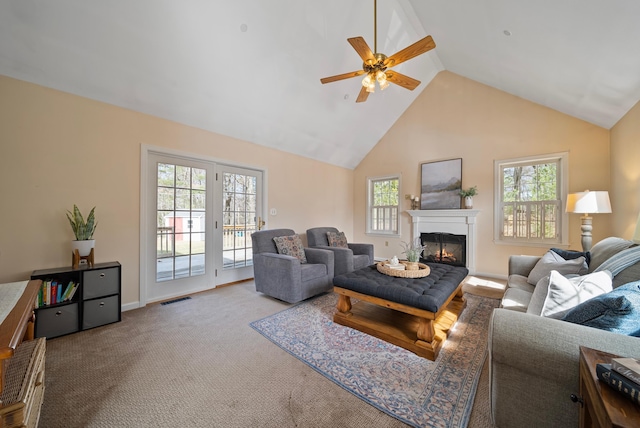 carpeted living area featuring visible vents, plenty of natural light, high vaulted ceiling, and a glass covered fireplace