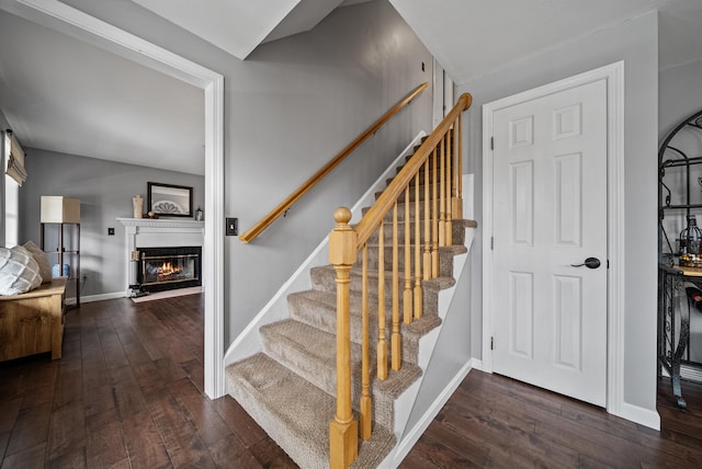 stairs featuring baseboards, wood-type flooring, and a glass covered fireplace