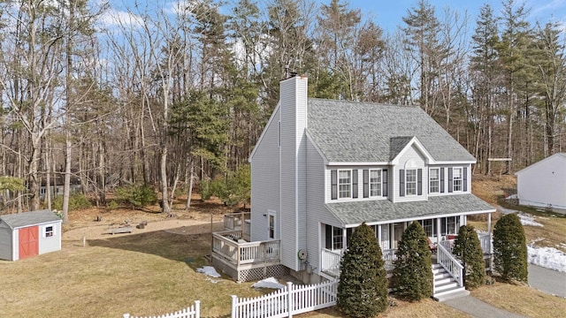 view of front of house with a shingled roof, fence, a front yard, an outdoor structure, and a storage unit