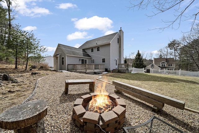 back of house featuring fence, an outdoor fire pit, a lawn, a chimney, and a deck