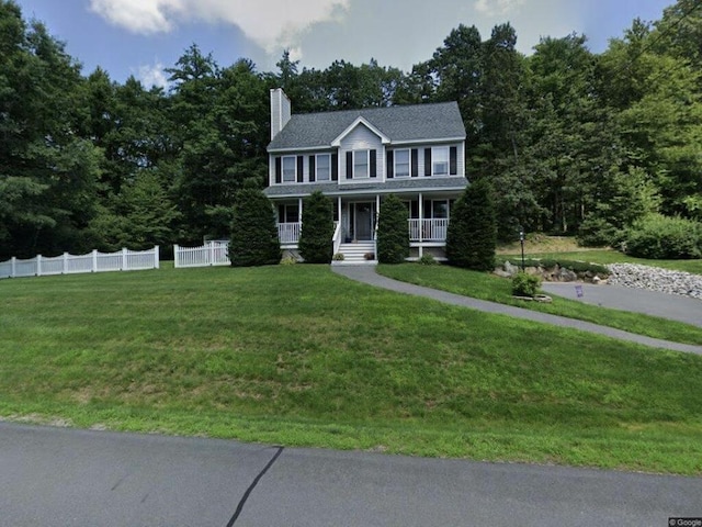 colonial inspired home featuring a porch, a chimney, a front yard, and fence