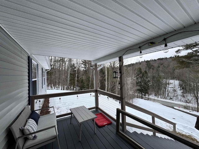 snow covered deck featuring a wooded view