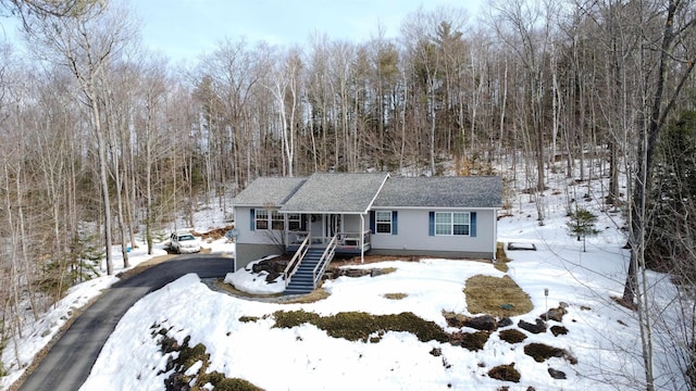 single story home featuring aphalt driveway, a porch, stairway, roof with shingles, and a wooded view