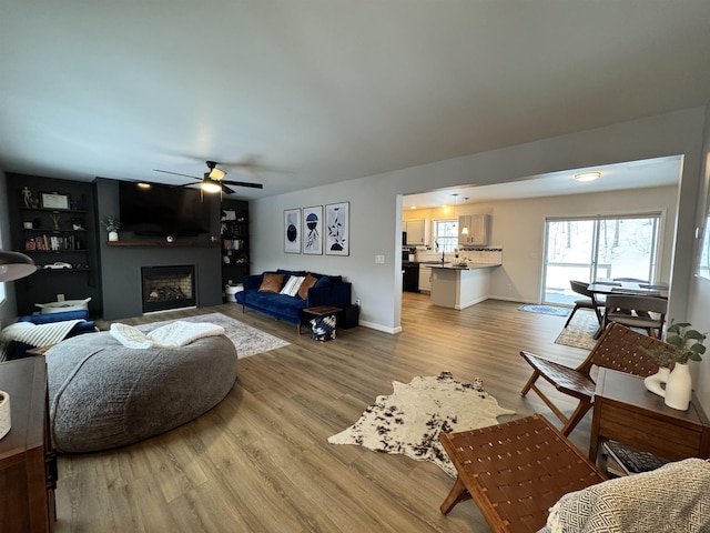 living room featuring a ceiling fan, a fireplace, light wood-type flooring, and baseboards