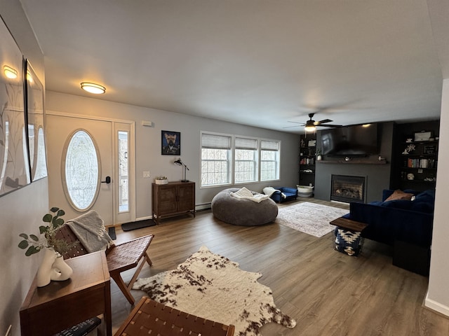 living area with a baseboard heating unit, wood finished floors, a fireplace, baseboards, and ceiling fan