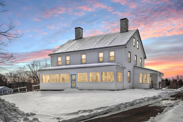 back of property at dusk with a chimney and a sunroom