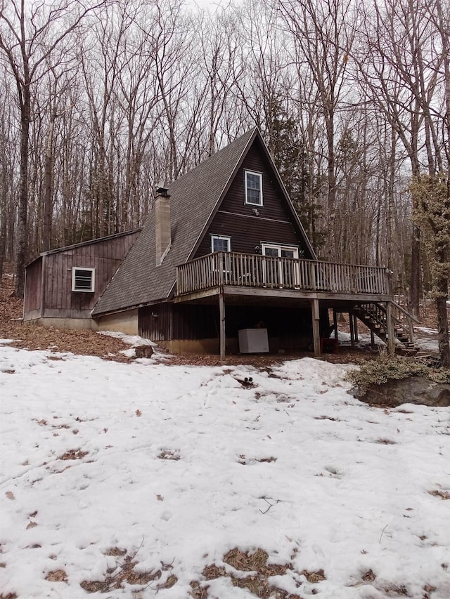 snow covered back of property featuring stairs, a garage, a deck, and a chimney