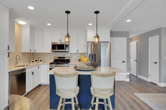 kitchen featuring a sink, stainless steel appliances, light wood-style floors, white cabinetry, and tasteful backsplash