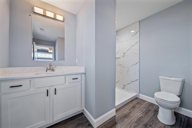 bathroom with vanity, wood finished floors, baseboards, a marble finish shower, and toilet