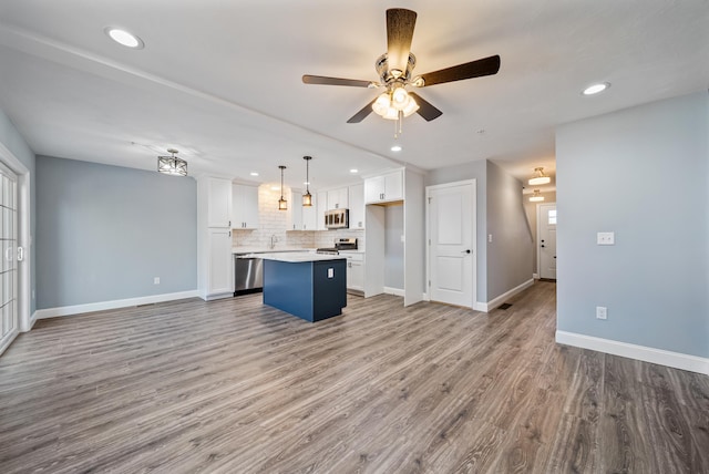 kitchen with a center island, open floor plan, stainless steel appliances, wood finished floors, and white cabinetry