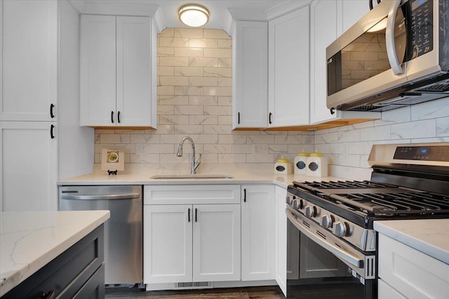 kitchen with white cabinets, appliances with stainless steel finishes, light stone countertops, and a sink