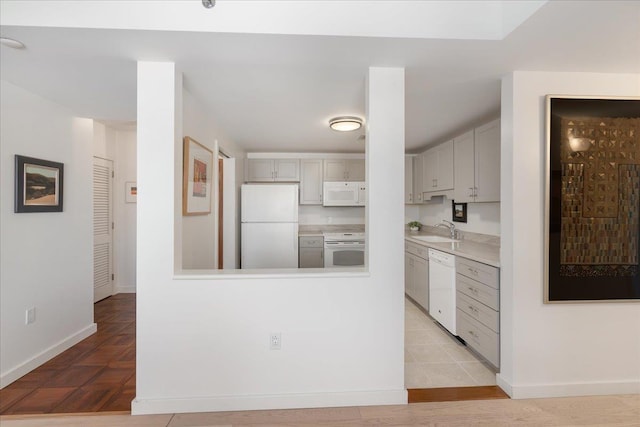 kitchen featuring gray cabinets, a sink, white appliances, light countertops, and baseboards