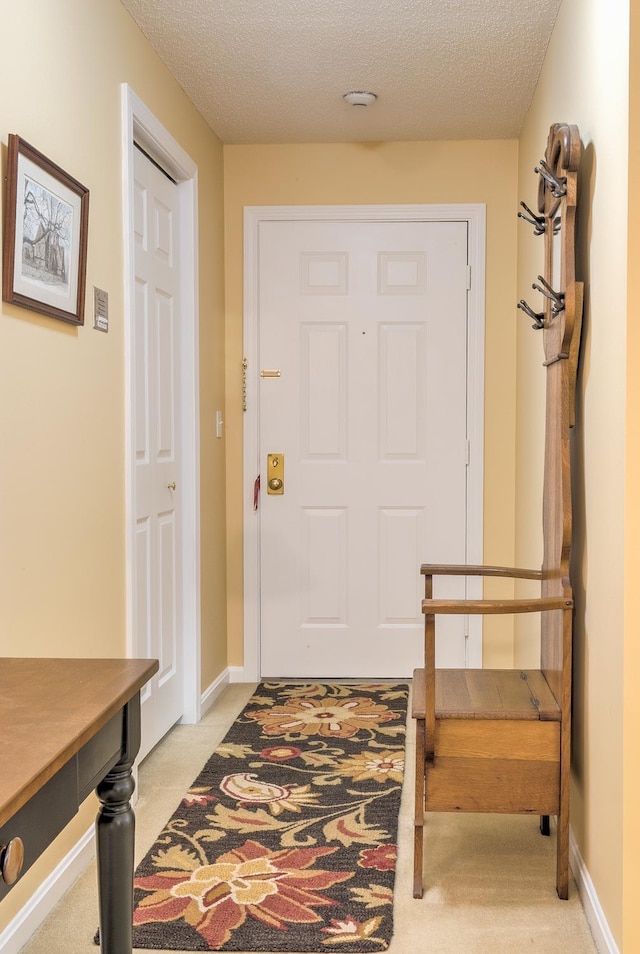 entryway with light colored carpet, a textured ceiling, and baseboards