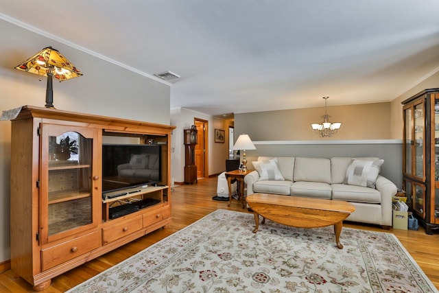 living area with visible vents, wood finished floors, a chandelier, and ornamental molding