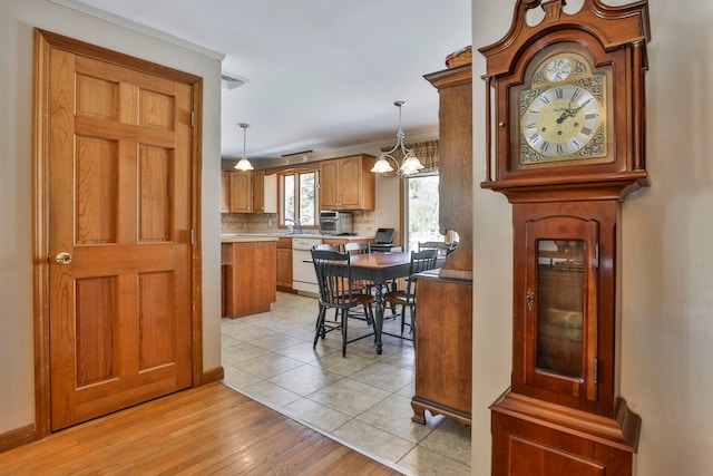 kitchen with tasteful backsplash, visible vents, light wood-style floors, white dishwasher, and hanging light fixtures