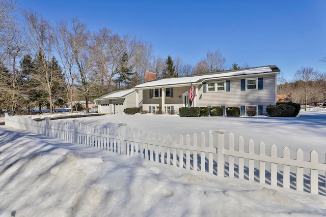 split foyer home featuring a fenced front yard, a garage, and a chimney