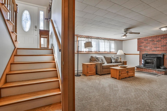 living area featuring stairway, a wood stove, carpet flooring, and a baseboard radiator