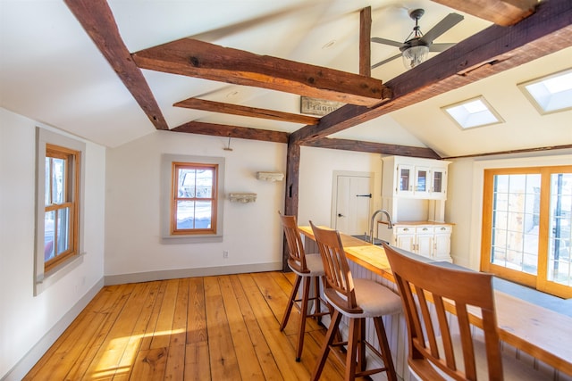 dining room featuring ceiling fan, baseboards, lofted ceiling with beams, and light wood-style floors