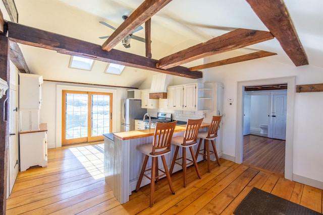 kitchen featuring decorative backsplash, vaulted ceiling with skylight, appliances with stainless steel finishes, and light wood finished floors