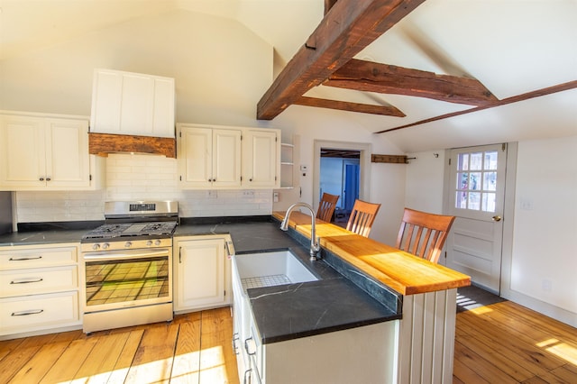 kitchen with a peninsula, lofted ceiling with beams, stainless steel range with gas stovetop, and a sink