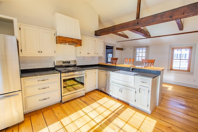 kitchen with lofted ceiling with beams, decorative backsplash, appliances with stainless steel finishes, a peninsula, and a sink