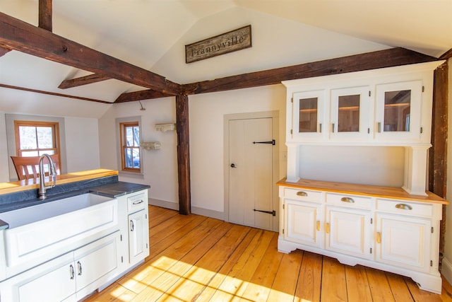 kitchen with vaulted ceiling, white cabinets, light wood-type flooring, and a sink