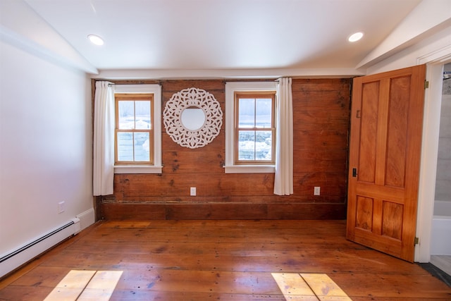 empty room with a baseboard heating unit, plenty of natural light, hardwood / wood-style flooring, and vaulted ceiling