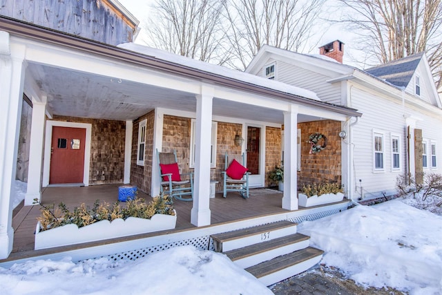 snow covered property entrance with a porch and a chimney